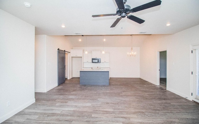 unfurnished living room featuring ceiling fan with notable chandelier, light hardwood / wood-style floors, and a barn door