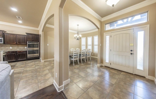 foyer entrance with light tile patterned floors, crown molding, and a notable chandelier