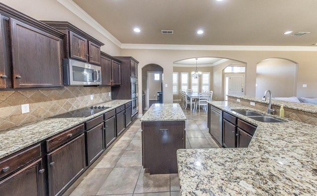 kitchen with sink, appliances with stainless steel finishes, a center island, light stone countertops, and decorative backsplash