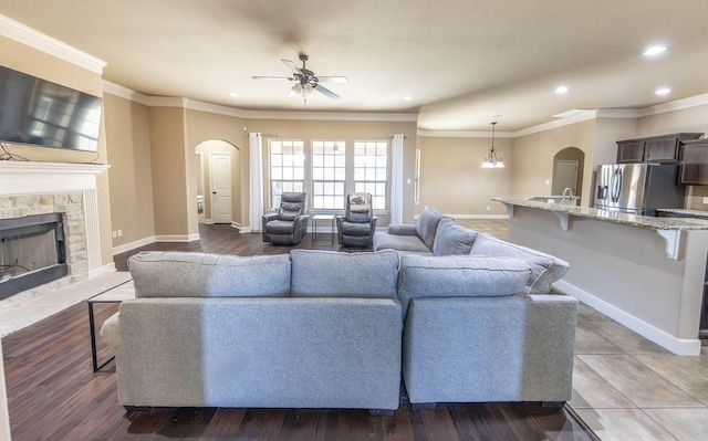 living room featuring crown molding, ceiling fan, wood-type flooring, and a stone fireplace