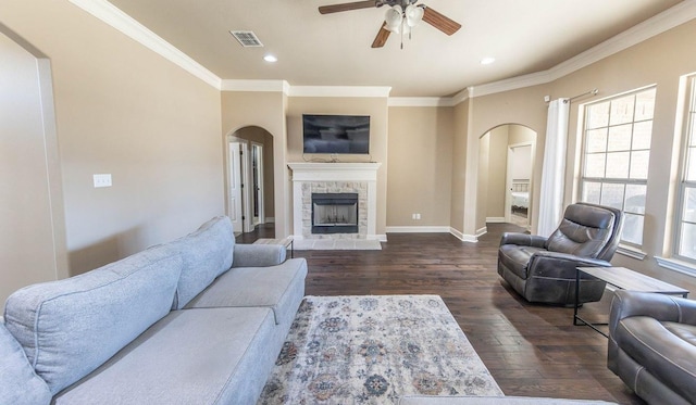 living room with crown molding, a stone fireplace, dark hardwood / wood-style floors, and ceiling fan