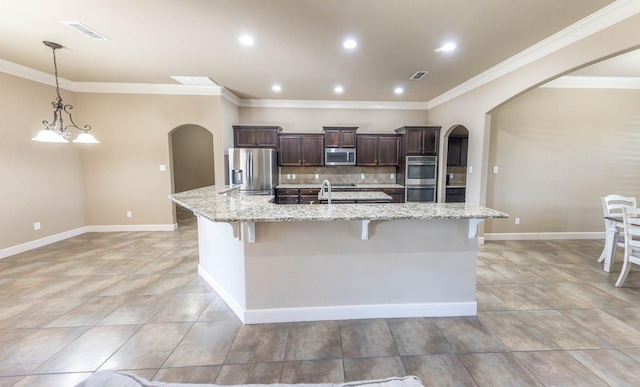 kitchen featuring appliances with stainless steel finishes, hanging light fixtures, a kitchen breakfast bar, light stone countertops, and a large island with sink