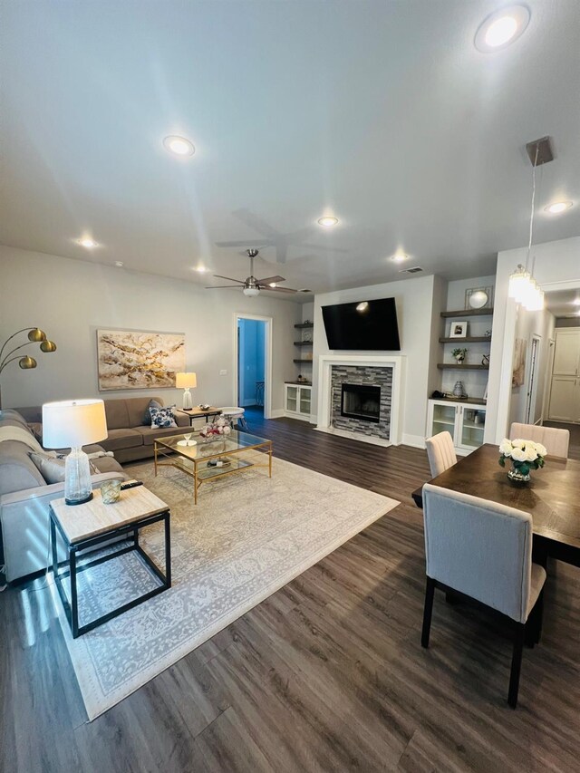 living room featuring dark wood-type flooring, ceiling fan, and a tiled fireplace