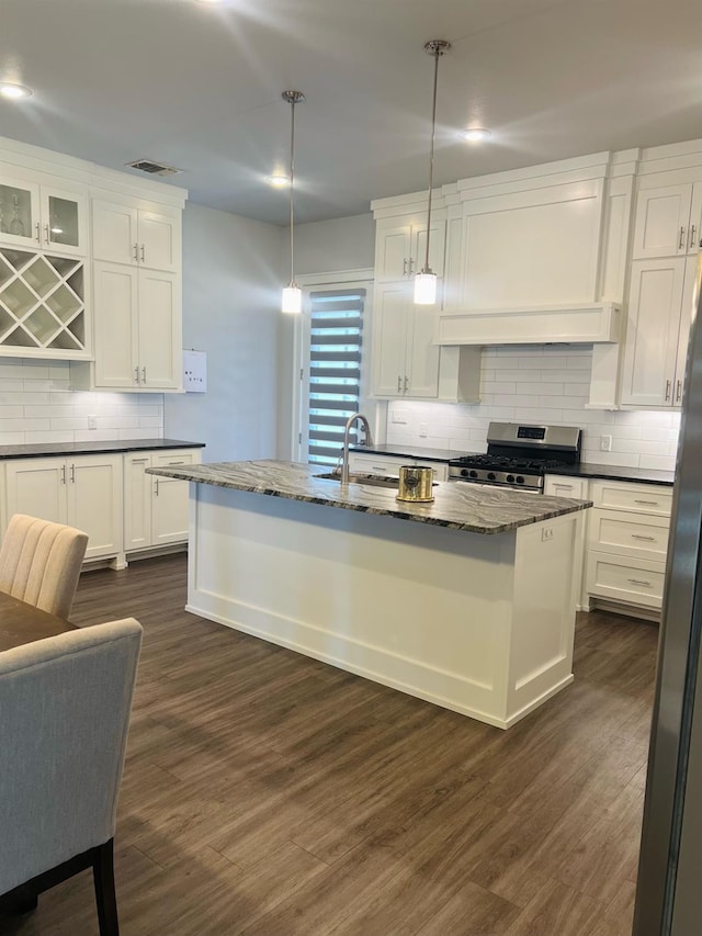 kitchen featuring pendant lighting, stainless steel appliances, an island with sink, and white cabinets