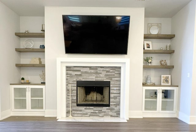 unfurnished living room with a tiled fireplace, hardwood / wood-style floors, and built in shelves