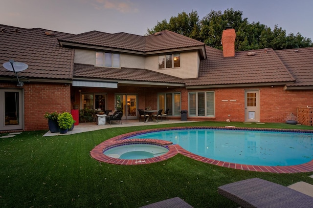 back house at dusk with a swimming pool with hot tub, a patio, and a yard