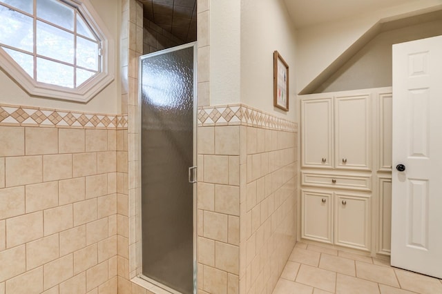 bathroom with a shower with shower door, tile patterned flooring, and tile walls