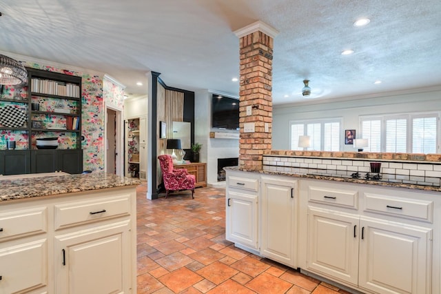 kitchen featuring stone counters, crown molding, decorative columns, and a textured ceiling