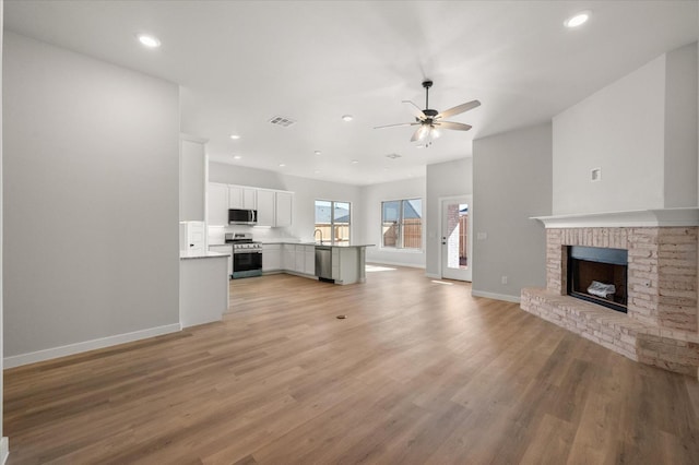 unfurnished living room featuring ceiling fan, a fireplace, sink, and light wood-type flooring