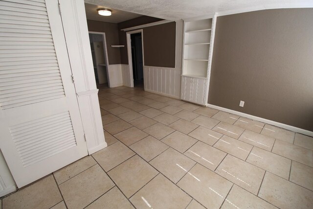 spare room featuring light tile patterned flooring, built in shelves, and a textured ceiling