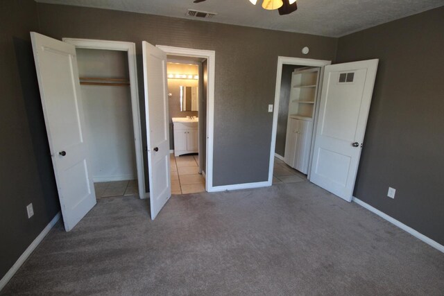 unfurnished bedroom with ensuite bath, light colored carpet, a closet, and ceiling fan