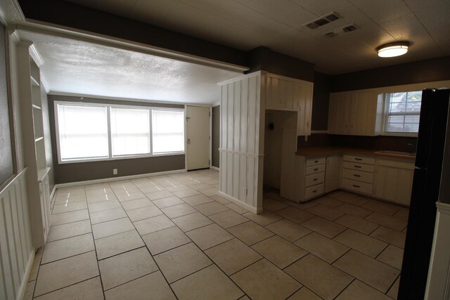 kitchen with light tile patterned floors, cream cabinets, a textured ceiling, and black fridge