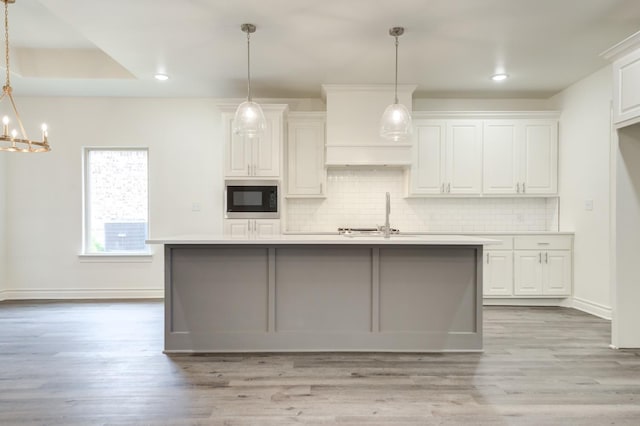 kitchen featuring white cabinetry, hanging light fixtures, black microwave, a center island with sink, and decorative backsplash