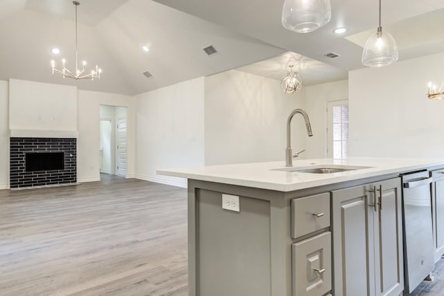 kitchen with decorative light fixtures, lofted ceiling, sink, a chandelier, and a center island with sink