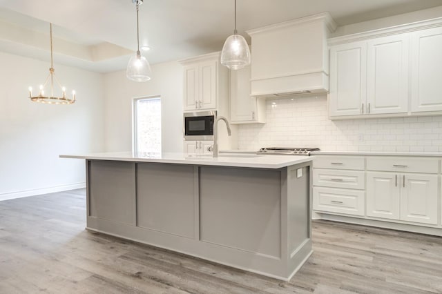 kitchen with white cabinetry, premium range hood, decorative light fixtures, and a center island with sink