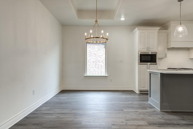 kitchen with white cabinetry, wood-type flooring, built in microwave, decorative backsplash, and a raised ceiling