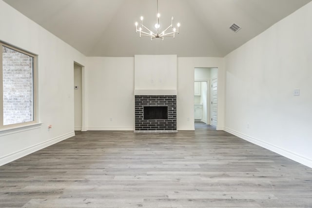 unfurnished living room featuring a chandelier, a tiled fireplace, high vaulted ceiling, and light hardwood / wood-style flooring