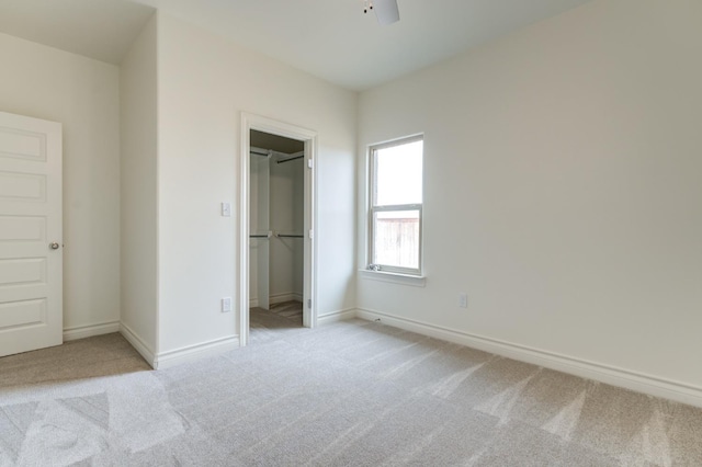 unfurnished bedroom with a walk in closet, light colored carpet, ceiling fan, and a closet