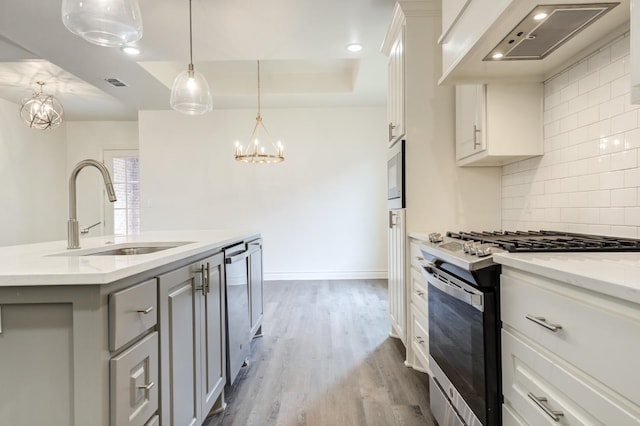 kitchen featuring sink, custom exhaust hood, white cabinetry, appliances with stainless steel finishes, and an island with sink