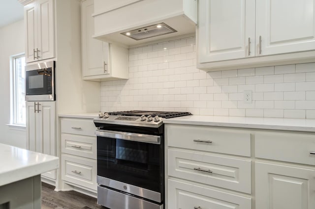 kitchen featuring appliances with stainless steel finishes, dark hardwood / wood-style floors, custom range hood, white cabinets, and backsplash