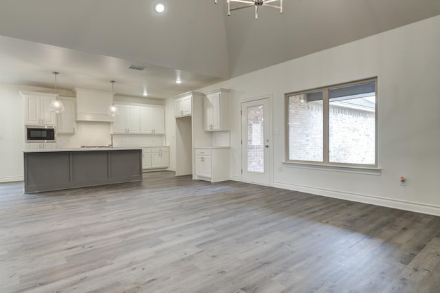 unfurnished living room featuring a towering ceiling, sink, and light wood-type flooring