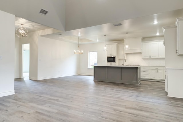 kitchen featuring hanging light fixtures, a center island with sink, white cabinets, and light hardwood / wood-style flooring