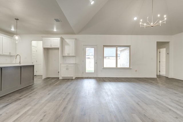 unfurnished living room featuring lofted ceiling, sink, a chandelier, and light hardwood / wood-style floors