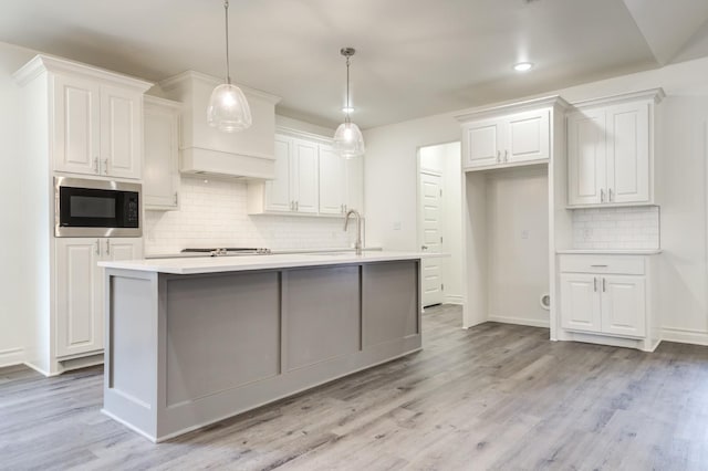 kitchen featuring pendant lighting, a kitchen island with sink, light hardwood / wood-style floors, white cabinets, and built in microwave