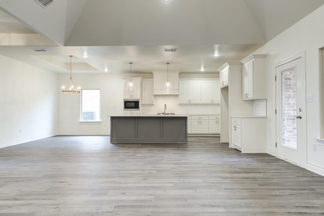 kitchen with pendant lighting, sink, white cabinetry, black microwave, and a center island with sink