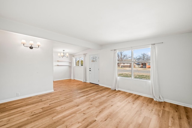 spare room with beam ceiling, an inviting chandelier, and light hardwood / wood-style flooring