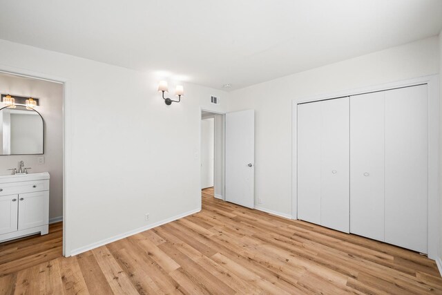 unfurnished bedroom featuring ensuite bathroom, sink, light wood-type flooring, and a closet