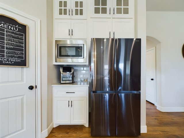 kitchen featuring stainless steel appliances, dark wood finished floors, backsplash, and glass insert cabinets