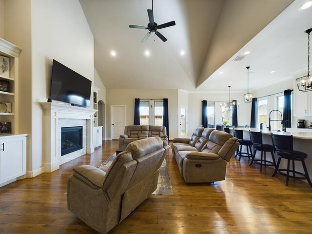 living area with visible vents, a towering ceiling, dark wood-style floors, a fireplace, and ceiling fan with notable chandelier