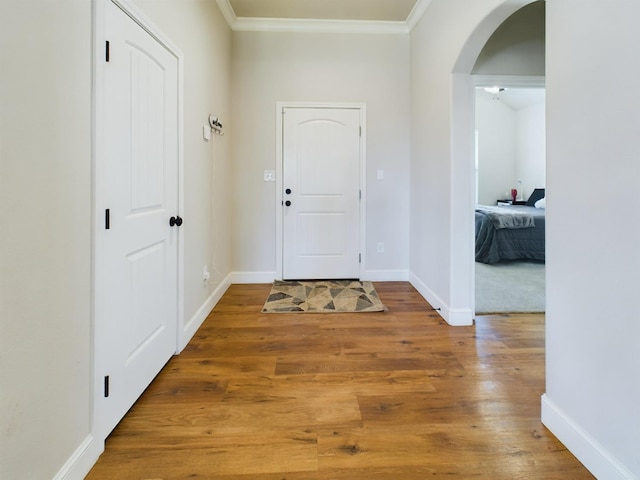 foyer entrance featuring arched walkways, crown molding, baseboards, and wood finished floors