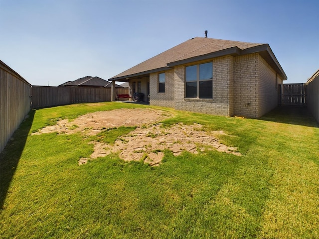 rear view of house featuring brick siding, a fenced backyard, and a yard