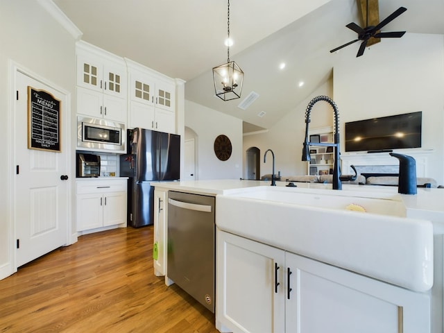 kitchen with light wood finished floors, arched walkways, white cabinets, appliances with stainless steel finishes, and a sink