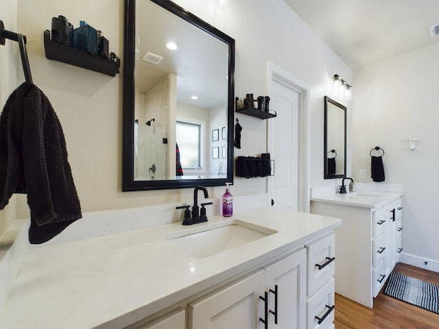 full bath with two vanities, a sink, a shower stall, and wood finished floors