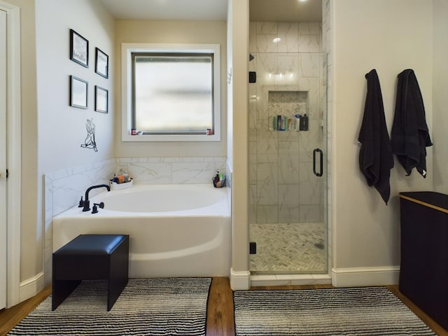 bathroom featuring wood finished floors, a shower stall, baseboards, and a bath