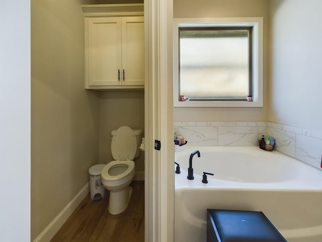 bathroom with baseboards, a garden tub, toilet, and wood finished floors