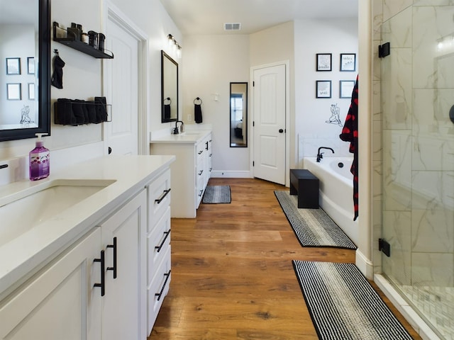 full bathroom featuring visible vents, wood finished floors, a sink, a shower stall, and two vanities