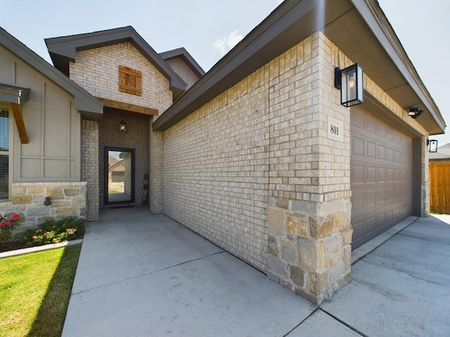 doorway to property featuring driveway, an attached garage, and brick siding