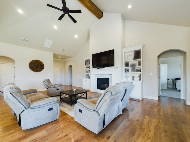 living room featuring arched walkways, a fireplace, wood finished floors, high vaulted ceiling, and beamed ceiling