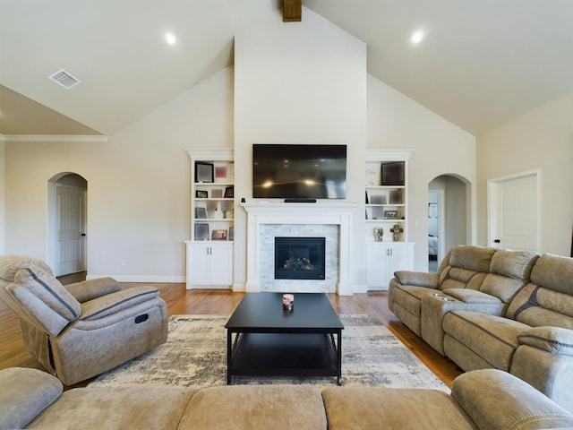 living room with arched walkways, high vaulted ceiling, wood finished floors, visible vents, and a glass covered fireplace