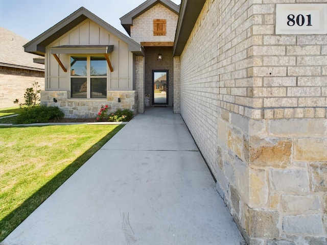 entrance to property featuring stone siding, a yard, board and batten siding, and brick siding