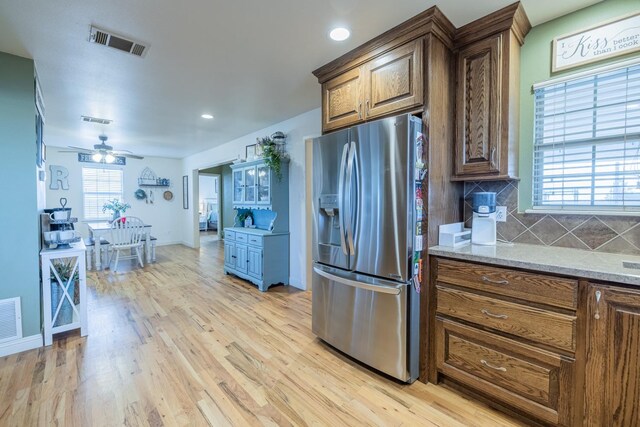 kitchen featuring light stone counters, tasteful backsplash, light wood-type flooring, stainless steel fridge, and ceiling fan