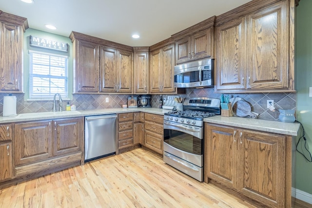 kitchen with decorative backsplash, appliances with stainless steel finishes, sink, and light hardwood / wood-style flooring