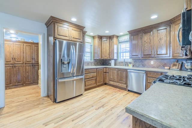 kitchen with tasteful backsplash, sink, light hardwood / wood-style floors, and appliances with stainless steel finishes