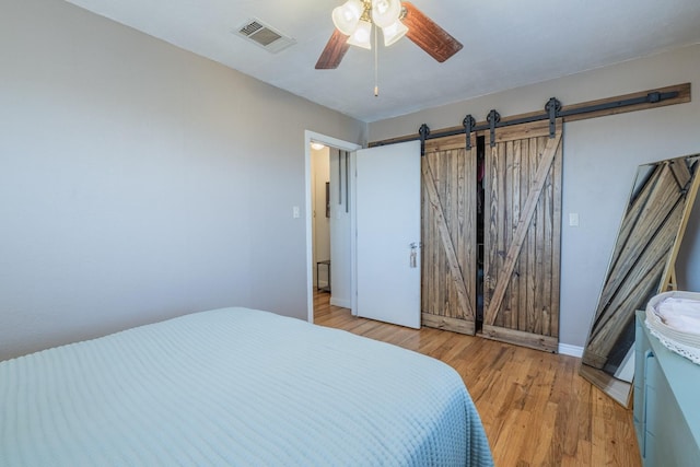 bedroom with a barn door, ceiling fan, and light hardwood / wood-style flooring