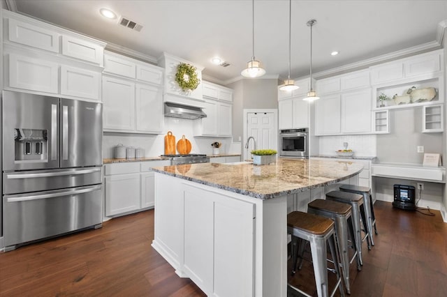 kitchen featuring appliances with stainless steel finishes, pendant lighting, white cabinets, light stone countertops, and a center island with sink