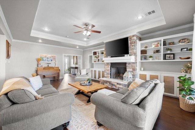 living room featuring hardwood / wood-style flooring, ceiling fan, a tray ceiling, and a stone fireplace